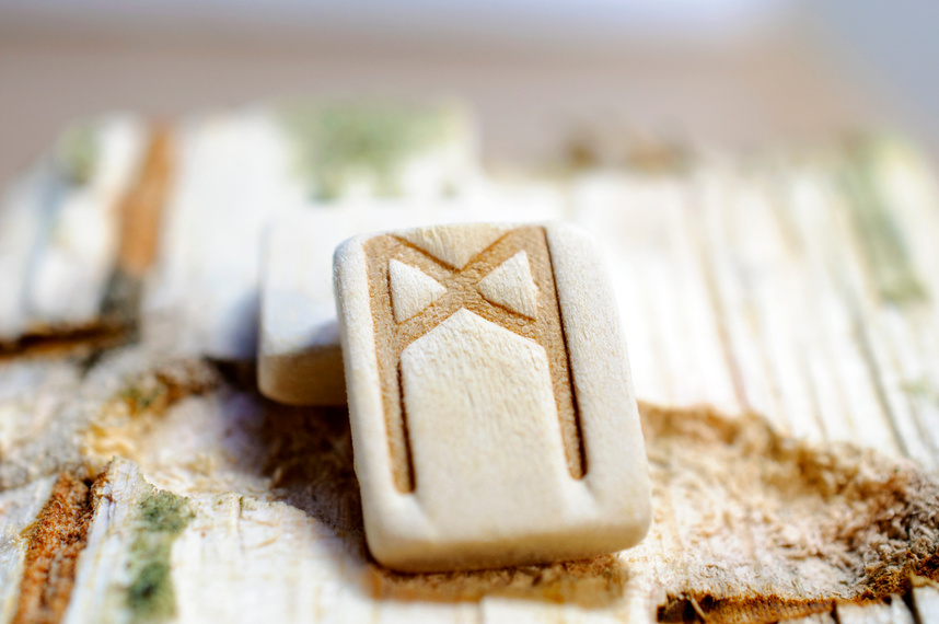 Wooden rune Mannaz close up on a wooden background. Soft focus